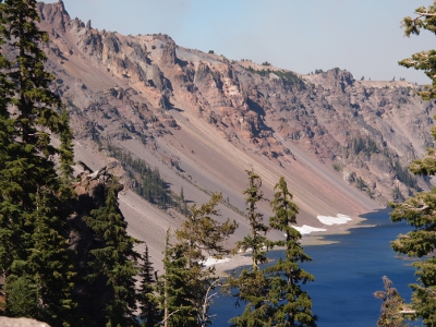 [Grey-pink stone edges of the crater take up most of the photo. At the lowest edge of the crater just before the water are white patches of snow.]